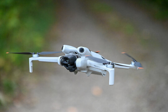 drone de loisirs en vol sur un fond de v&eacute;g&eacute;tation et de verdure. Mod&egrave;le DJI mini 4 pro avec cam&eacute;ra et nacelle, les 4 h&eacute;lices tournent au bout des bras pliables.