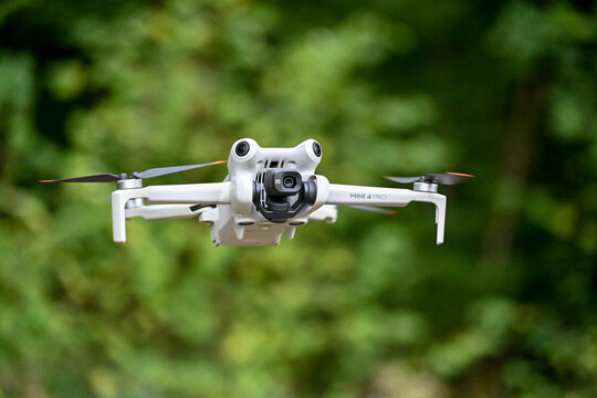 drone de loisirs en vol sur un fond de v&eacute;g&eacute;tation et de verdure. Mod&egrave;le DJI mini 4 pro avec cam&eacute;ra et nacelle, les 4 h&eacute;lices tournent au bout des bras pliables.