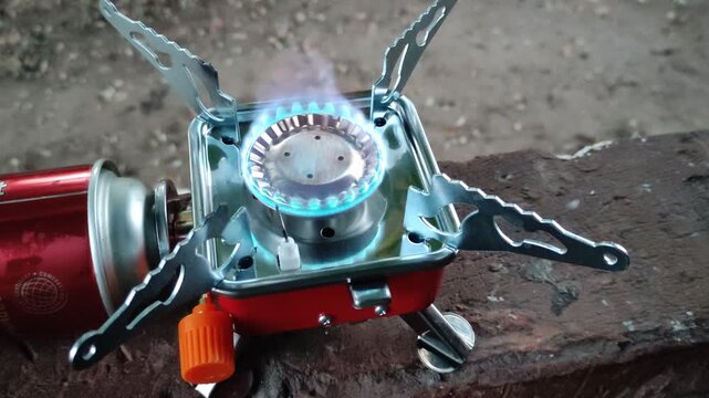 Portable camping gas stove with blue flame burning on a brick surface outdoors