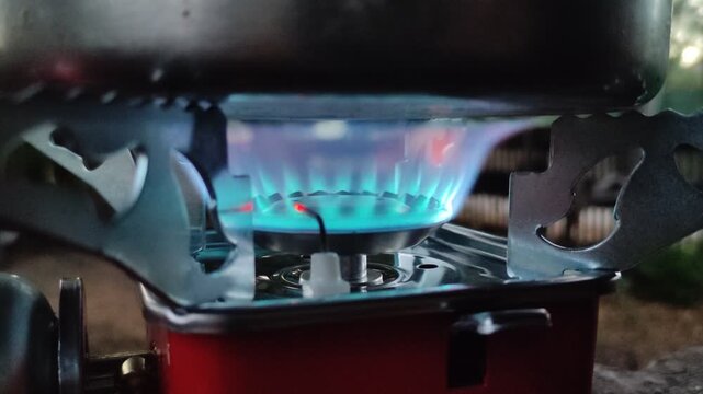 Close up of a portable camping gas stove with blue flame burning under a pot