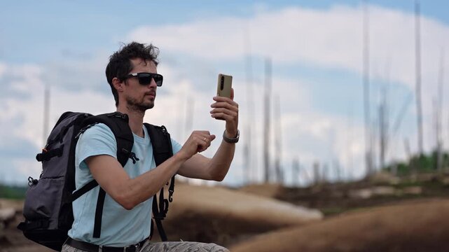 Traveler with backpack photographing wild nature using smartphone, enjoying peaceful freedom and open exploration