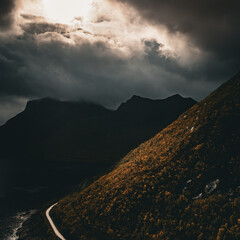 Aerial view of a winding coastal road along a colorful autumn mountain slope and fjord under dramatic sky with copy space © Quality by Simon