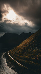 Aerial view of a winding coastal road along a colorful autumn mountain slope and fjord under dramatic sky with copy space © Quality by Simon