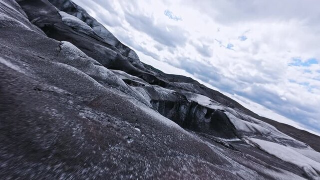 Dynamic FPV drone flight skimming above and between deep glacier crevasses on glacier, Iceland. Cinematic aerial footage revealing blue ice formations and dramatic glacial landscape.