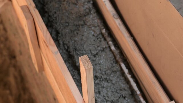 Pouring concrete mortar into wooden foundation formwork. Close-up of fresh cement mixture inside formwork, symbolizing the foundation construction process and creating a strong base