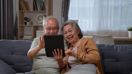 Senior Asian couple use a tablet touchscreen together at home, showing elderly husband and wife...