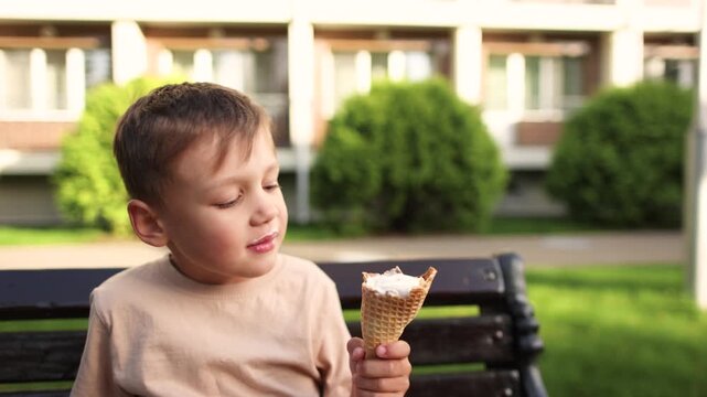 Boy bites soft waffle cone while eating ice cream during summer. Flexible wafer stretches slightly during bite showing texture of softened dessert cone.