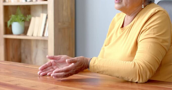 Close up of people talking to the camera, senior woman in yellow sweater sitting at wooden table