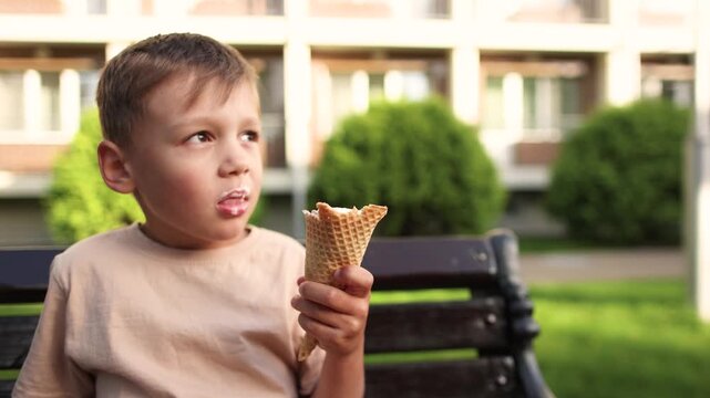 Boy with changing baby teeth eats ice cream and grimaces during bite. Cold dessert helps soothe tender gums while child experiences temporary discomfort.