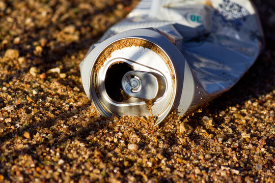Discarded crushed aluminum beverage can lying on gritty sandy beach ground, creating an environmental pollution hazard close-up view capturing the impact of human litter on nature outdoors