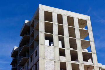 Modern high-rise building under construction featuring raw concrete skeleton frames against a vibrant clear blue sky, emphasizing urban architectural development and structural engineering progress © PhotoChur
