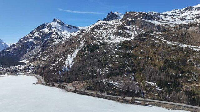 sils maria lakeside village chalets frozen silsersee shoreline engadin valley switzerland alpine road winds along shore winter snowy granite peaks aerial drone flight