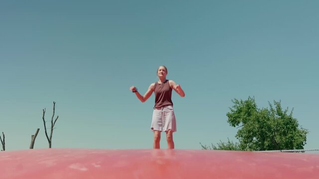 A girl is doing the splits on a trampoline outdoors slow motion