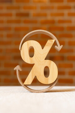 Loan refinancing and interest rate cycle concept, wooden percentage sign encircled by curved arrows on table against brick wall, symbolizing debt restructuring, renewal, and turnover.