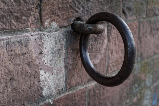 Rusty metal ring attached to a brick wall in a rural setting during daylight