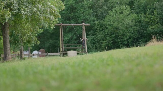 The boy jump on a zip line rope swing low angle slow motion outdoors