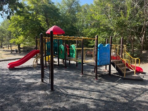 Colorful children playground equipment with slides and monkey bars in a public park surrounded by green trees on a sunny day