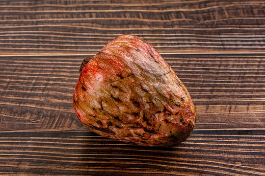 Ripe annona fruit with textured red and green skin resting on dark wood surface