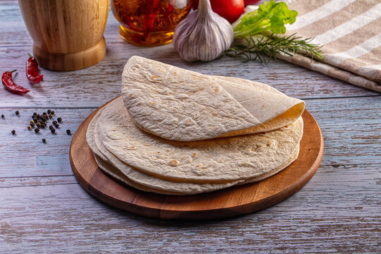 Fresh flatbread on a wooden board with garlic, chili peppers, and herbs on a rustic table