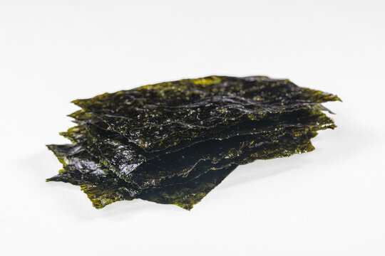 Stack of dark green nori sheets with glossy texture on white background, close up
