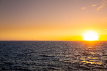 Fototapeta premium Golden sun setting over ocean horizon and coastal structures