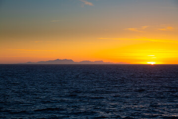 Fototapeta premium Golden sun setting over ocean horizon and coastal structures