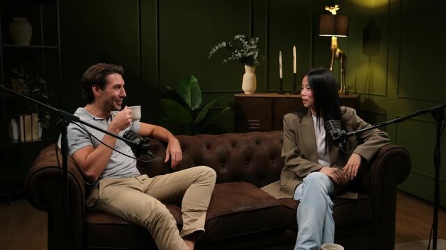 Caucasian man and an asian woman discussing during a podcast recording session in a cozy studio