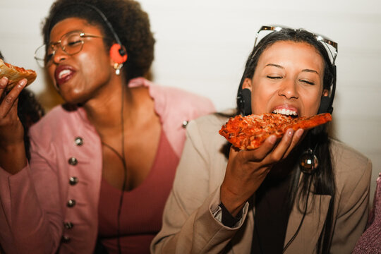 African american girls eating pizza outdoor in the streets after party concert - Food, people lifestyle and nightlife concept - Main focus on right young woman face - UGC flash content
