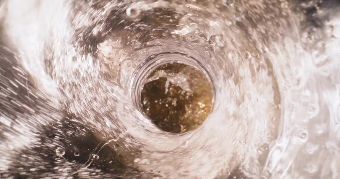 Slow motion water vortex draining down kitchen sink basin with stainless metal surface. top down tracking shot, probe view.