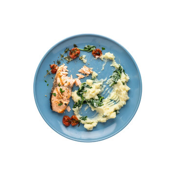 Unfinished grilled salmon and mashed potatoes on a blue plate isolated. Partially eaten seafood dinner leftovers with spinach and roasted tomatoes. Top down view of remaining food scraps.