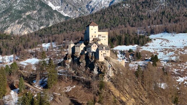 schloss tarasp castle crowns rocky outcrop above larch forest snowcapped mountains rise beyond stone keep tower dominates skyline lower engadin switzerland drone aerial view
