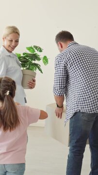 Family parents children unpacking boxes at home. Father lifts a carton as mother and daughters explore an empty room. Useful for relocation and homeowner campaigns. Fresh start for family life.