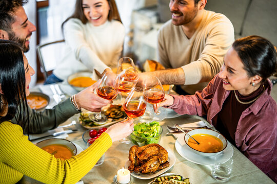 Happy friends toasting red wine on sitting at dinner table - Group of young people dining at home together