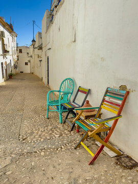 Colorful chairs and a small table line a charming cobblestone street with white buildings under a clear blue sky in the historic old town of Altea, Alicante, Spain - stock photo
