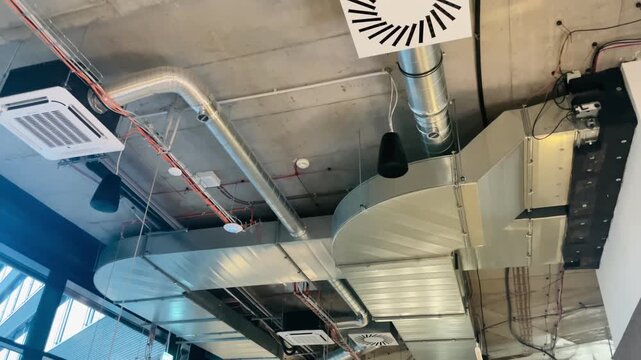 Industrial ceiling with ducts, HVAC vents and metal pipes, concrete slab texture and suspended pendant lights, modern loft office atmosphere Video taken on mobile device.