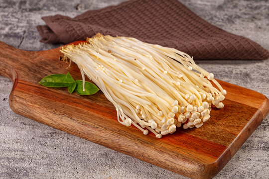 Fresh enoki mushrooms on wooden cutting board with green basil leaves, rustic kitchen background, soft natural lighting