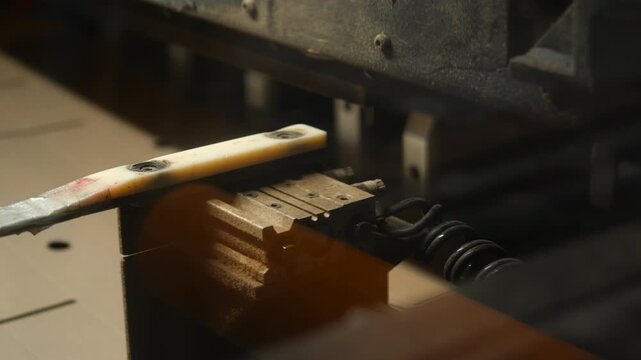 Blurred industrial machine mechanism with weathered metal block, pale handle, coiled spring, and dusty workshop parts in motion