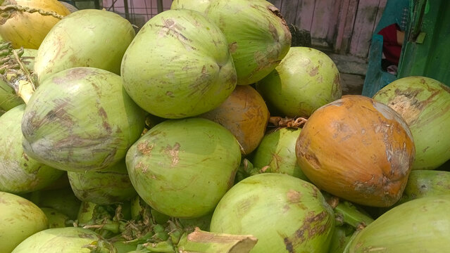 A vibrant cluster of fresh green and bright orange young coconuts piled together, showcasing rich tropical textures and natural summer colors. High-quality shot perfect for healthy lifestyle and bever