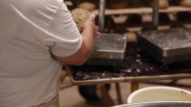 Hands work dense, dark rye bread dough inside a large wooden vessel, showing the rustic texture and traditional process of bread making