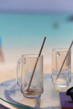 Empty drinking glasses with straws on a refreshment drink on a tropical beach summer background