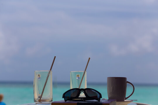 Empty drinking glasses with straws on a refreshment drink on a tropical beach summer background
