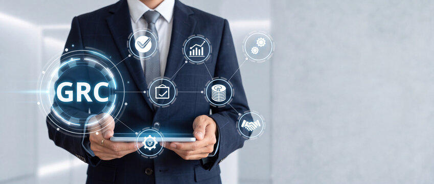 Businessman holding a tablet displaying a digital holographic GRC Governance Risk and Compliance interface with business icons for audit corporate management and data security standards