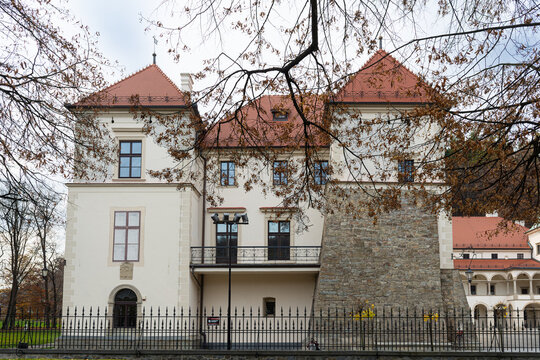 Sucha Beskidzka, Poland &ndash; November 2, 2025: Historic facade of Sucha Beskidzka Castle framed by autumn tree branches. White Renaissance walls, red tiled roofs, stone fortification and tall windows hig