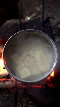 Close-up shot of boiling cassava inside a pot filled with bubbling water over a wood burning stove.
