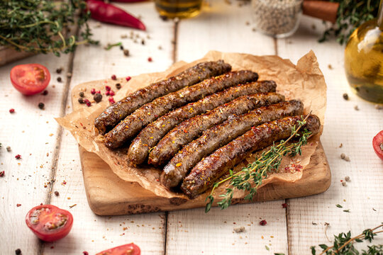 Juicy roasted grilled sausages served on parchment paper on wooden cutting board with herbs and spices