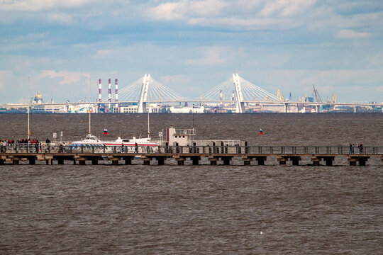 Scenic view of ZSD cable stayed bridge and Saint Isaac cathedral across dark gulf water on sunny day. Distant maritime city skyline from Peterhof pier near Saint Petersburg.