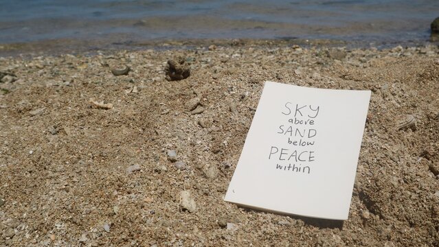 A handwritten inspirational quote on paper placed on a sandy beach shore.