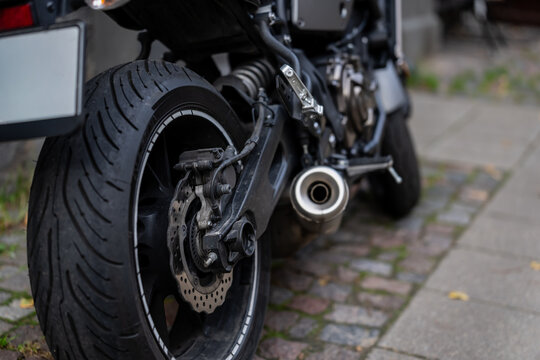 Motorcycle rear wheel with disc brake, caliper, swingarm and exhaust outlet, visible running gear components for two wheeler servicing and mechanical maintenance