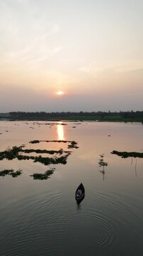 Small boat sails across calm river during golden sunset with beautiful reflections on water surface.