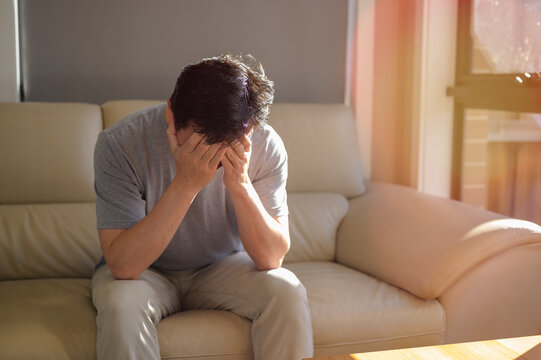 Stressed man reviewing bills and expenses at home while managing financial problems. Tired, headache and stress of man in living room with mental health, fatigue and sad problem